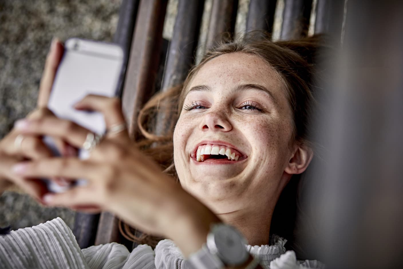 A happy woman lying down and holding her smartphone over her head.