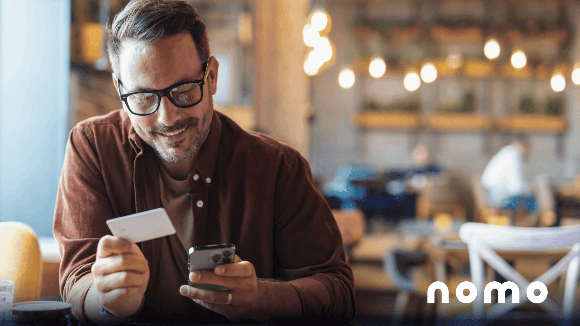 A bespectacled man holds a bank card and his mobile phone